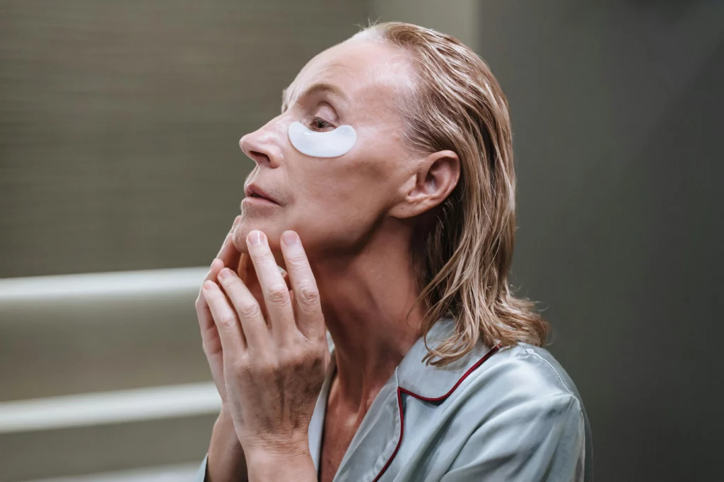 A middle-aged woman applying under-eye patches, highlighting the benefits of B2B argan oil products for anti-aging and skin hydration. Perfect for private-label skincare manufacturers.